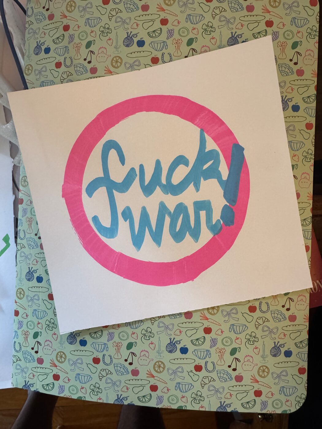 fuck war! in blue script inside a pink ring on a white sheet