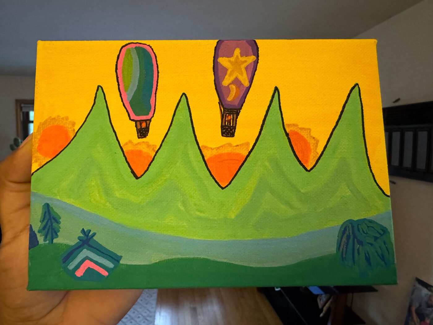 Painting on a small canvas: two hot-air balloons, one striped green and one purple with a star and a moon, over four green peaks with orange suns in a yellow sky, a river, trees and a tent below