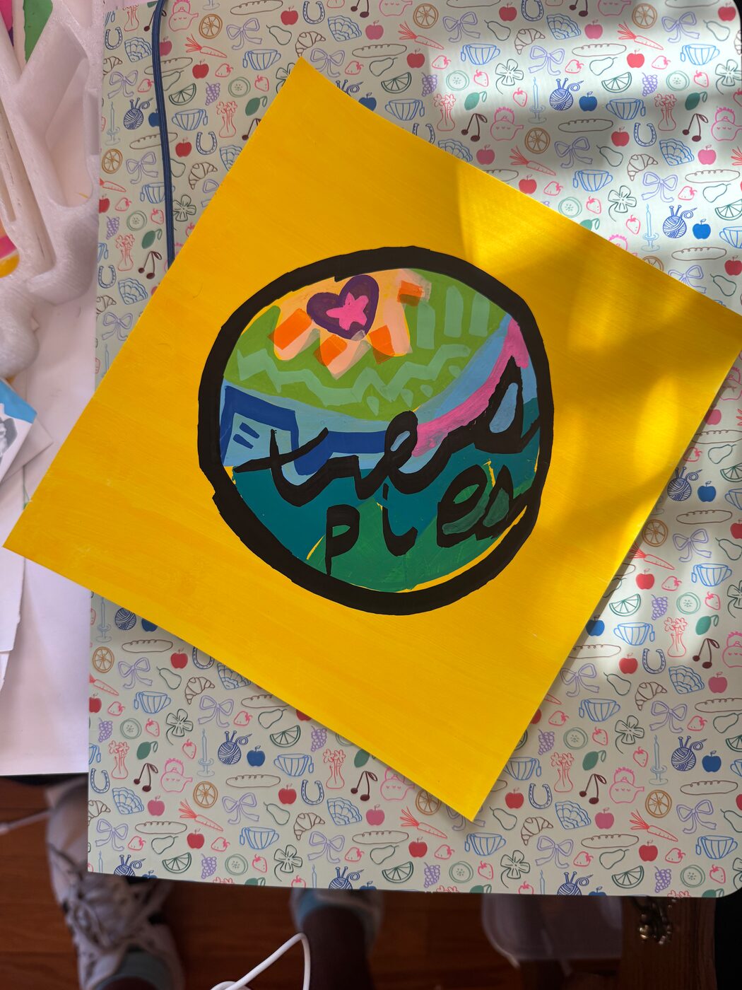 tres pies in black script across a painted disc of greens and blues, with a pink band and a purple heart around a pink star, on a yellow sheet