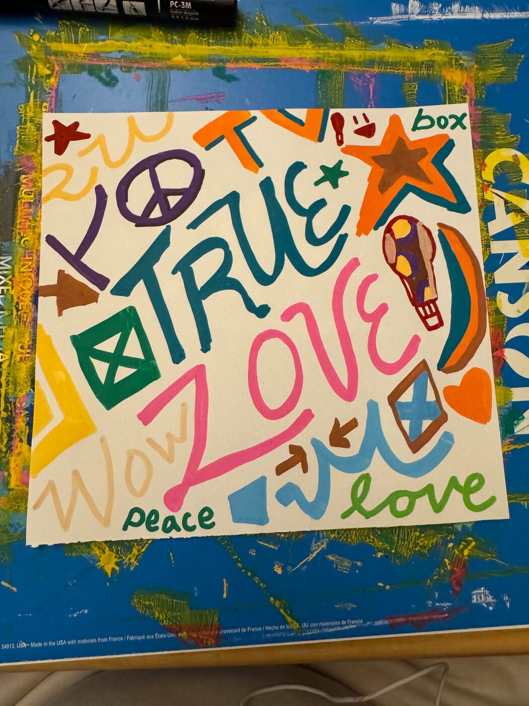 TRUE in teal and LOVE in pink on a sheet crowded with a peace sign, stars, a checked box, a small hot-air balloon, a heart, arrows, and the words peace, love, wow and box