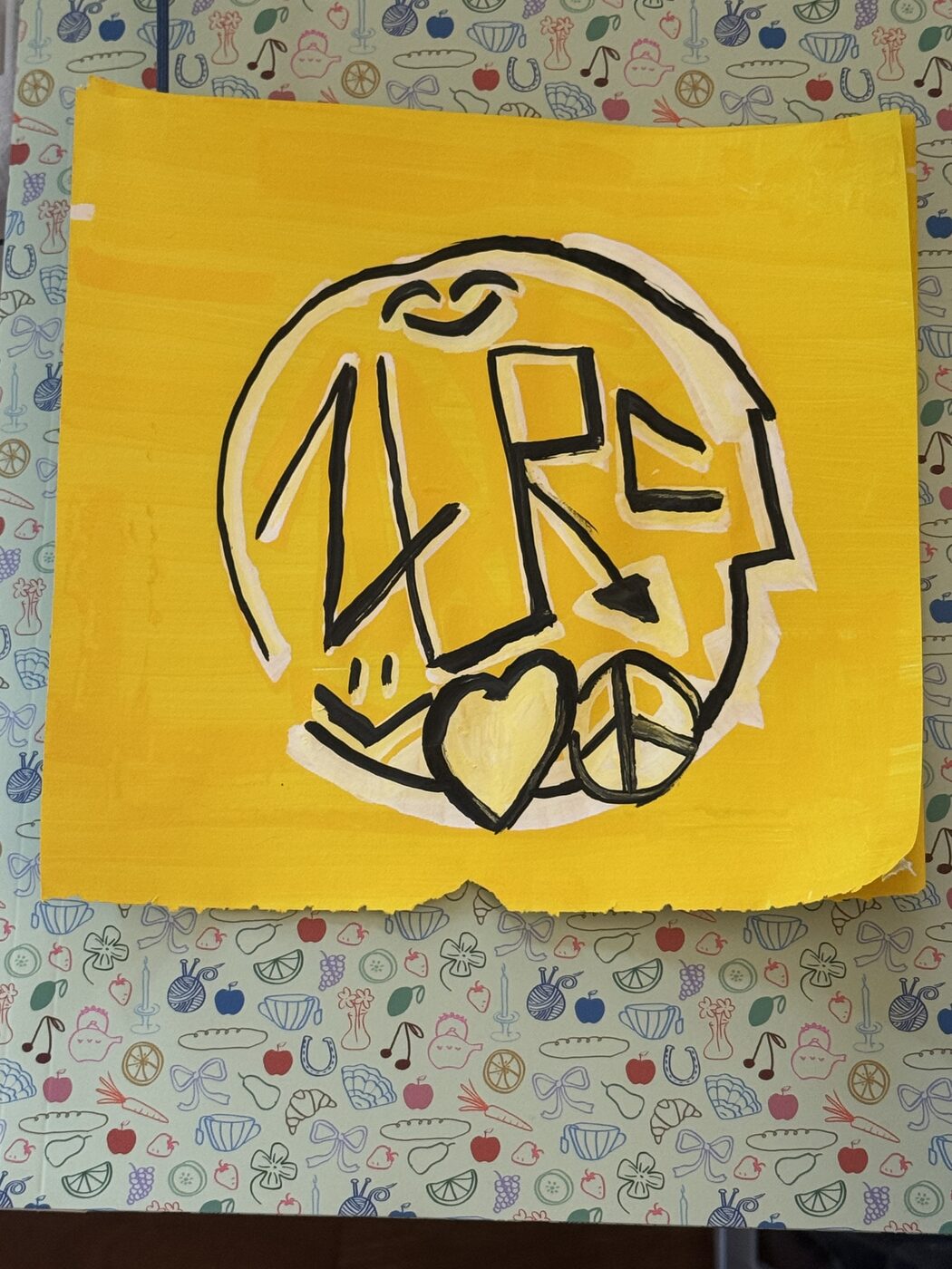ZURC in black marker on a yellow disc with a cream halo, with a heart and a peace sign, on a yellow sheet