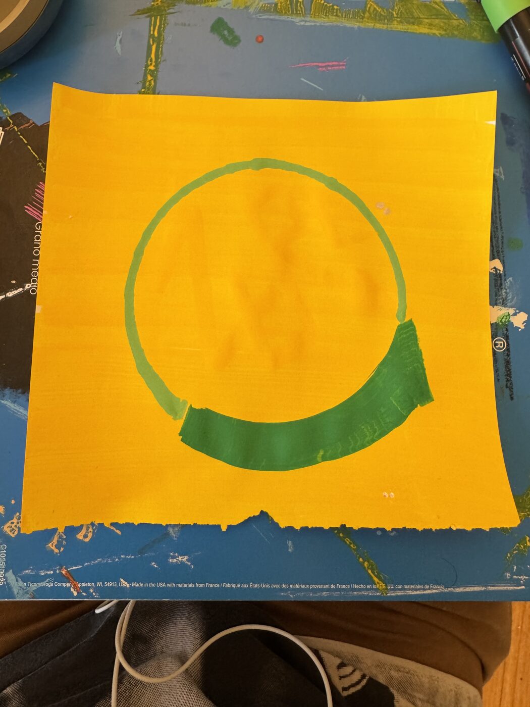 A green circle painted on a yellow sheet, the start of the ZURC mark, on a studio table