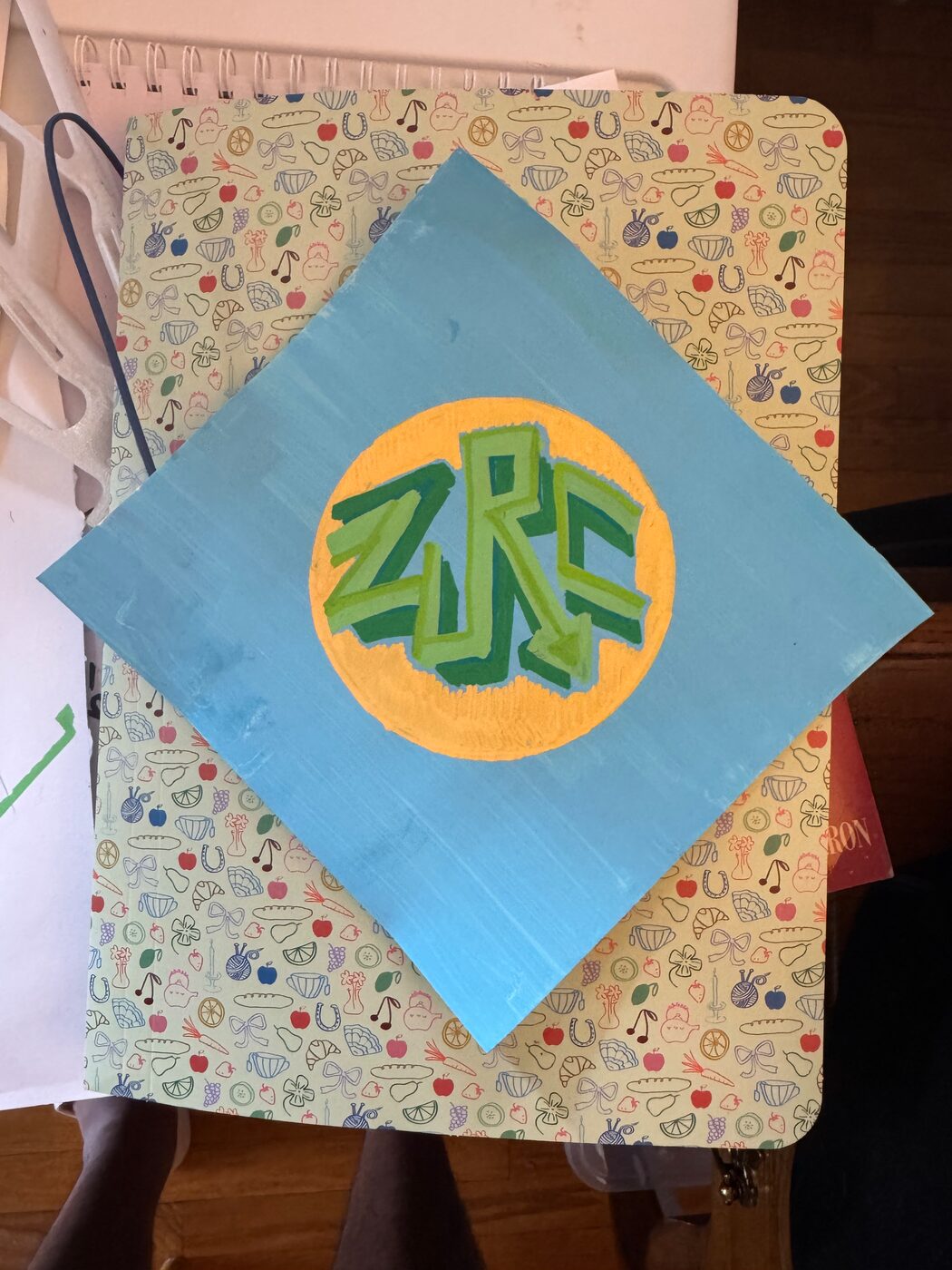 ZURC in green block letters with dark green shadows on a pale orange disc, on a light blue sheet turned on its point