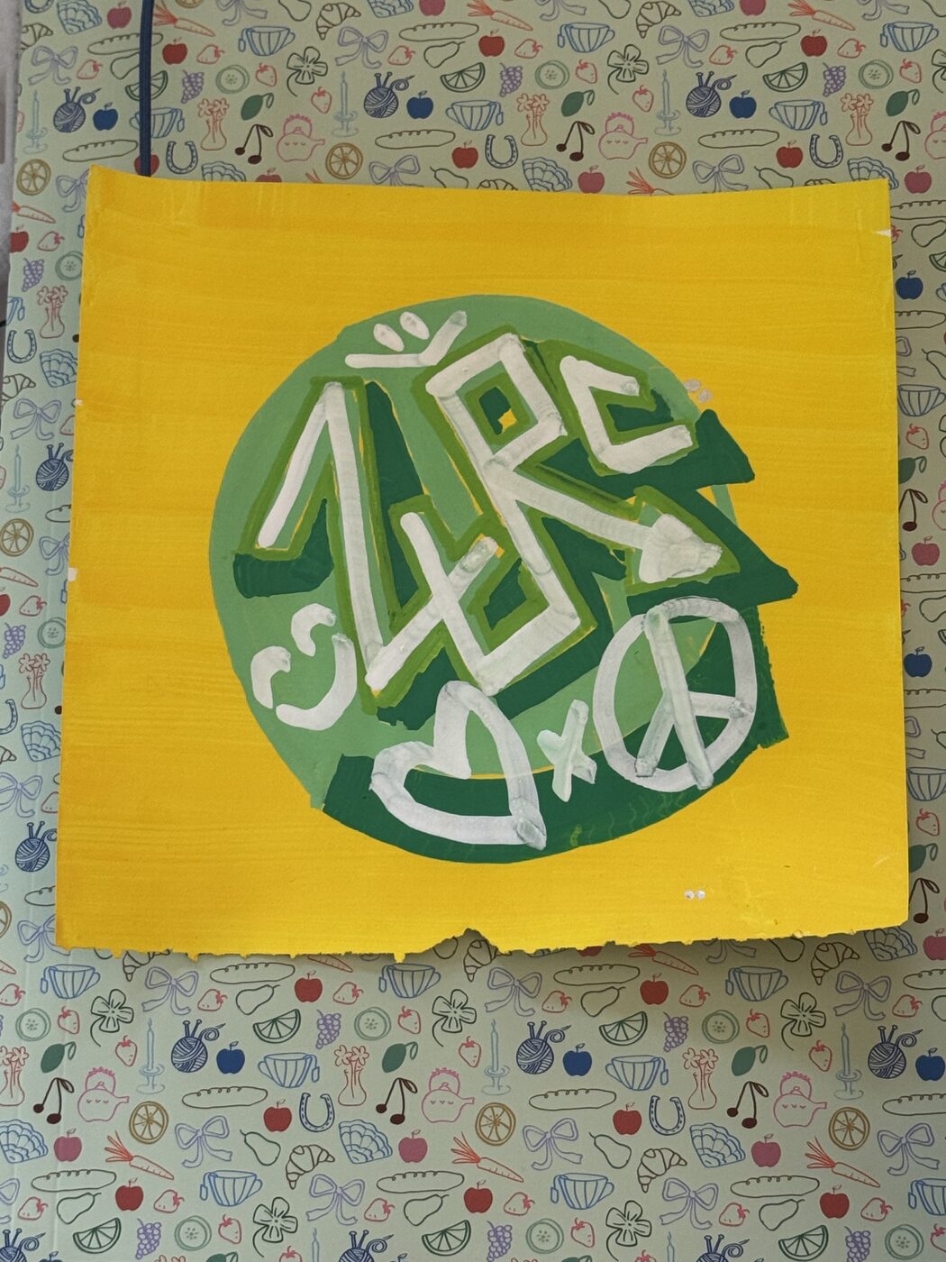 ZURC in white marker over a green disc on a yellow sheet, with a heart, an x, and a peace sign